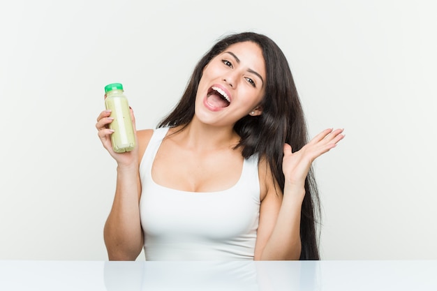 Jovem mulher hispânica segurando uma bebida vegetal comemorando uma vitória ou sucesso