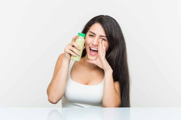 Jovem mulher hispânica segurando uma bebida vegetal gritando animado para a frente.