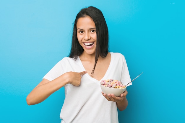 Foto jovem mulher hispânica, segurando uma tigela de cereal de açúcar surpreendeu apontando para si mesma