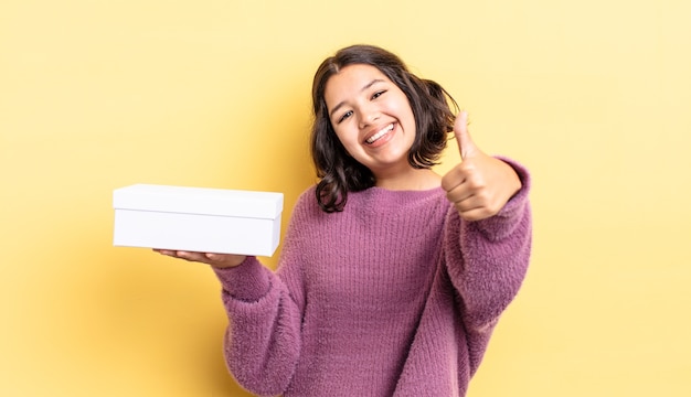 Jovem mulher hispânica, sentindo-se orgulhosa, sorrindo positivamente com o polegar para cima. conceito de caixa em branco