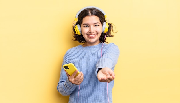 Jovem mulher hispânica, sorrindo alegremente com simpáticos e oferecendo e mostrando um conceito. conceito de fones de ouvido e smartphone