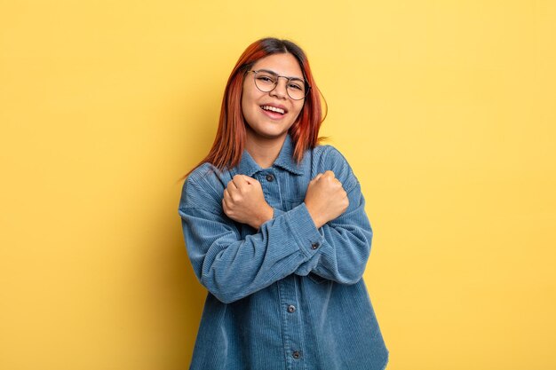 Foto jovem mulher hispânica sorrindo alegremente e comemorando, com os punhos cerrados e os braços cruzados, sentindo-se feliz e positivo