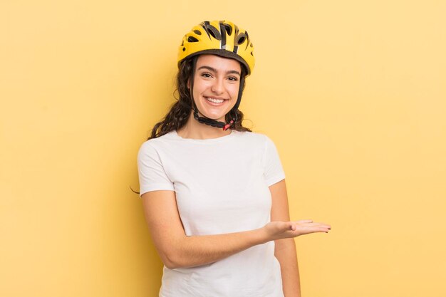 Jovem mulher hispânica sorrindo alegremente, sentindo-se feliz e mostrando um conceito de bicicleta de conceito