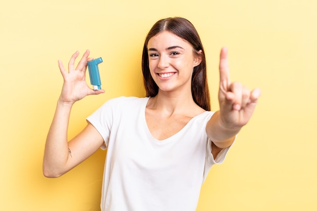 Jovem mulher hispânica sorrindo com orgulho e fazendo o número um com confiança. conceito de asma