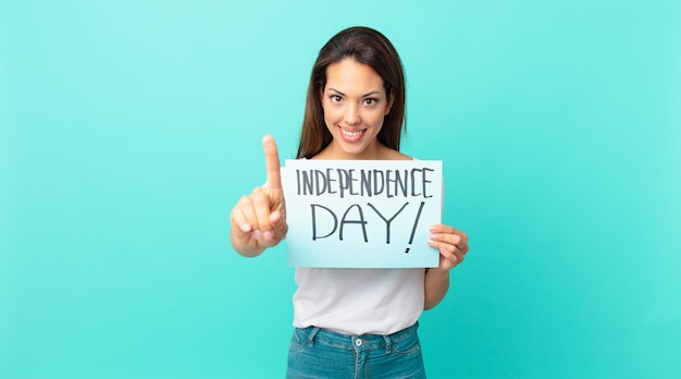 Jovem mulher hispânica sorrindo com orgulho e fazendo o número um com confiança. conceito do dia da independência