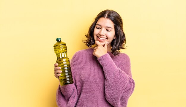 Jovem mulher hispânica sorrindo com uma expressão feliz e confiante com a mão no queixo. conceito de azeite