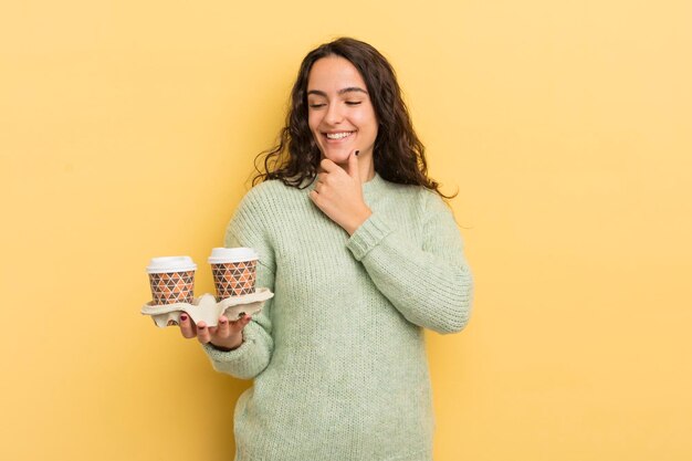 Jovem mulher hispânica sorrindo com uma expressão feliz e confiante com a mão no queixo tirar o conceito de café