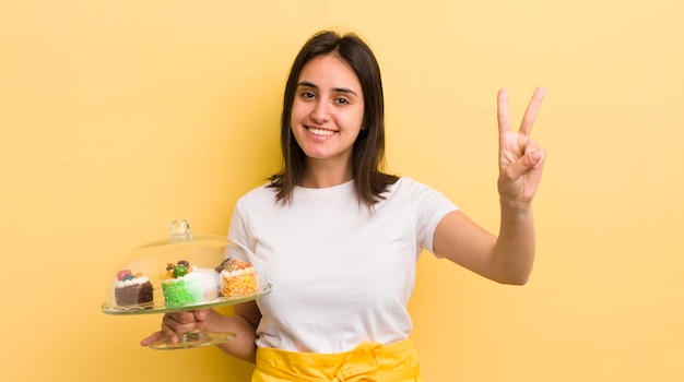 Foto jovem mulher hispânica sorrindo e olhando feliz gesticulando vitória ou paz conceito de bolos caseiros