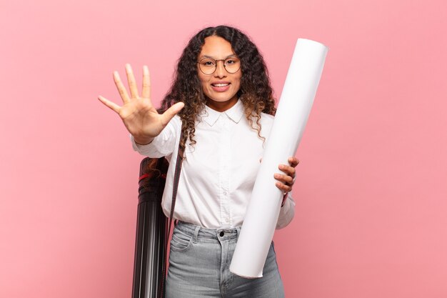 Jovem mulher hispânica sorrindo e parecendo amigável, mostrando o número cinco ou quinto com a mão para a frente, em contagem regressiva. conceito de arquiteto