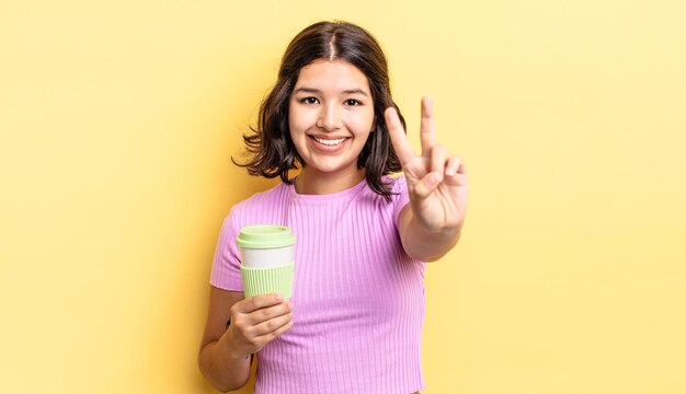 Jovem mulher hispânica sorrindo e parecendo amigável, mostrando o número dois. levar embora o conceito de café