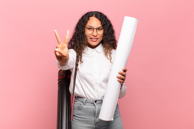 Jovem mulher hispânica sorrindo e parecendo amigável, mostrando o número dois ou o segundo com a mão para a frente, em contagem regressiva. conceito de arquiteto