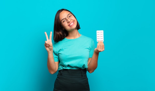 Jovem mulher hispânica sorrindo e parecendo amigável, mostrando o número dois ou o segundo com a mão para a frente, em contagem regressiva