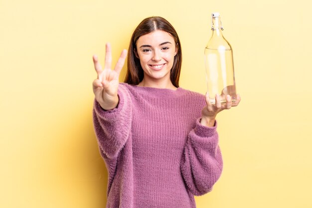 Jovem mulher hispânica sorrindo e parecendo amigável, mostrando o número três. conceito de garrafa de água