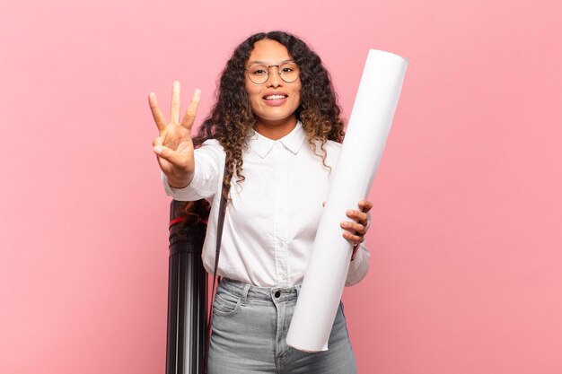 Jovem mulher hispânica sorrindo e parecendo amigável, mostrando o número três ou terceiro com a mão para a frente, em contagem regressiva. conceito de arquiteto