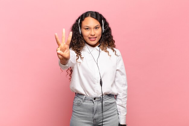 Foto jovem mulher hispânica sorrindo e parecendo amigável, mostrando o número três ou terceiro com a mão para a frente, em contagem regressiva. operador de telemarketing