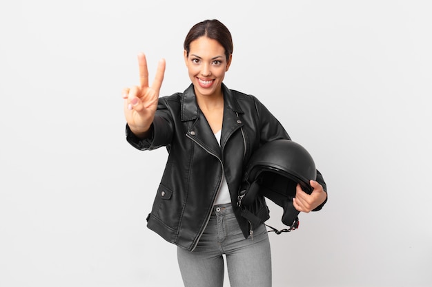 Jovem mulher hispânica sorrindo e parecendo feliz, gesticulando vitória ou paz. conceito de motociclista