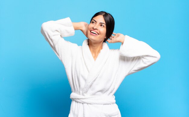 Jovem mulher hispânica sorrindo e sentindo-se relaxada, satisfeita e despreocupada, rindo positivamente e relaxando. conceito de roupão de banho