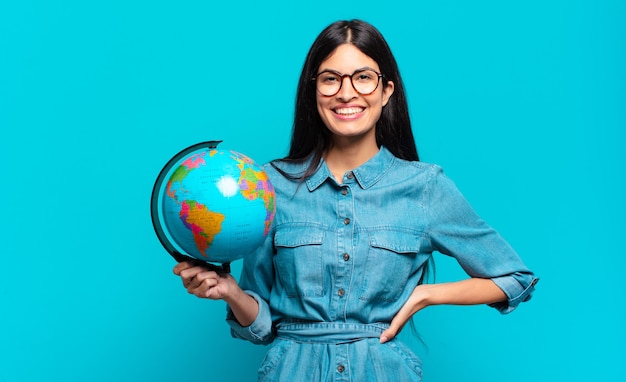 Jovem mulher hispânica sorrindo feliz com uma mão no quadril e uma atitude confiante, positiva, orgulhosa e amigável