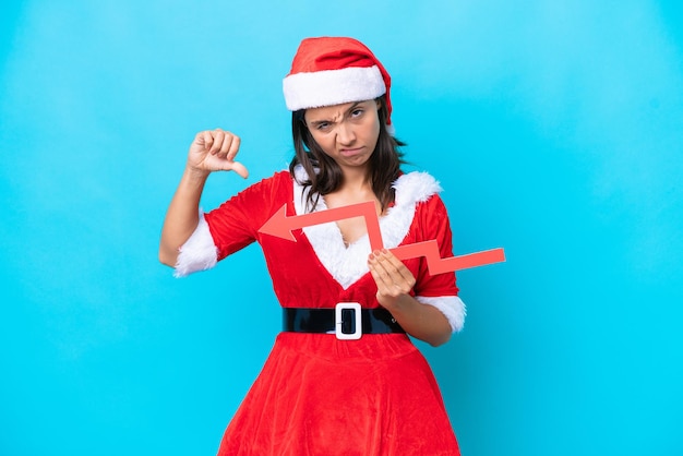 Foto jovem mulher hispânica vestida como mamãe noel isolada em fundo azul segurando uma seta para baixo e fazendo sinal ruim