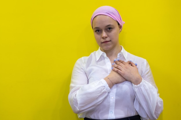 Jovem mulher hispânica vestindo câncer de mama apoia lenço rosa sorrindo com as mãos no peito e gesto grato no conceito de saúde do rosto