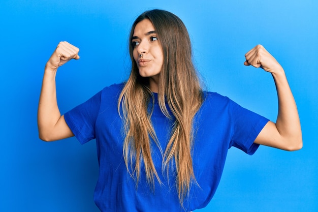 Jovem mulher hispânica vestindo roupas casuais, mostrando os músculos dos braços sorrindo orgulhoso. conceito de aptidão.