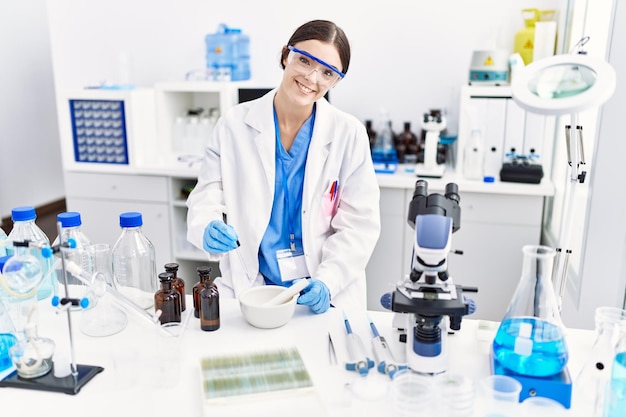 Jovem mulher hispânica vestindo uniforme de cientista trabalhando no laboratório