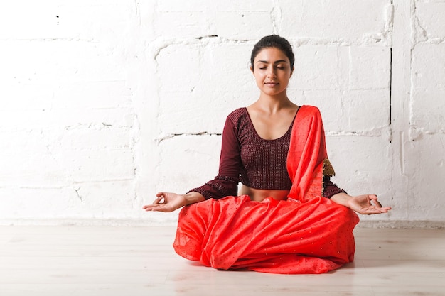 Jovem mulher indiana adulta em sari meditando ioga pose de lótus zen com sinal de ok gesto de mudra