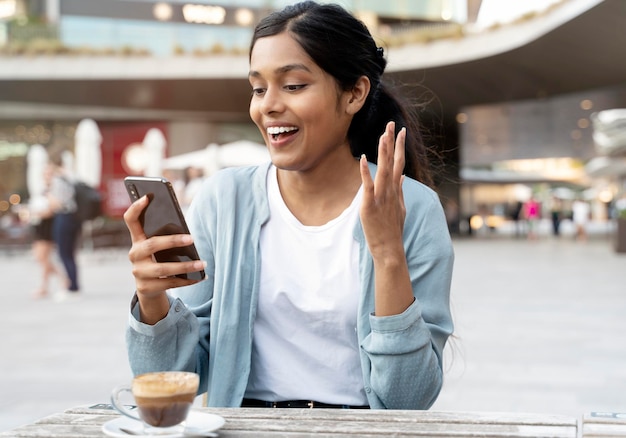 Jovem mulher indiana animada usando telefone celular fazendo compras on-line com venda sentada no café