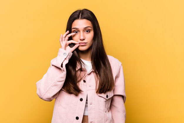 Jovem mulher indiana em amarelo com os dedos nos lábios, mantendo um segredo.