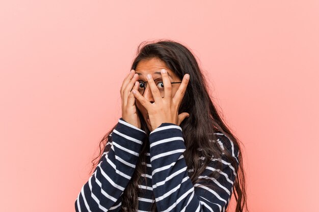 Jovem mulher indiana intelectual pisca entre os dedos, assustada e nervosa.