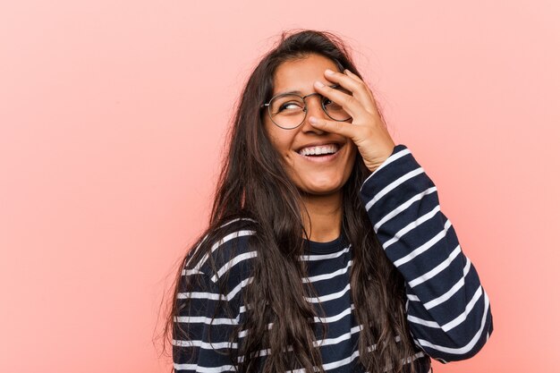 Jovem mulher indiana intelectual pisca para a câmera entre os dedos, com vergonha de cobrir o rosto.