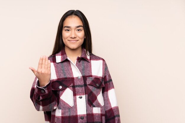 Jovem mulher indiana isolada em bege, convidando para vir com a mão. Feliz que você veio