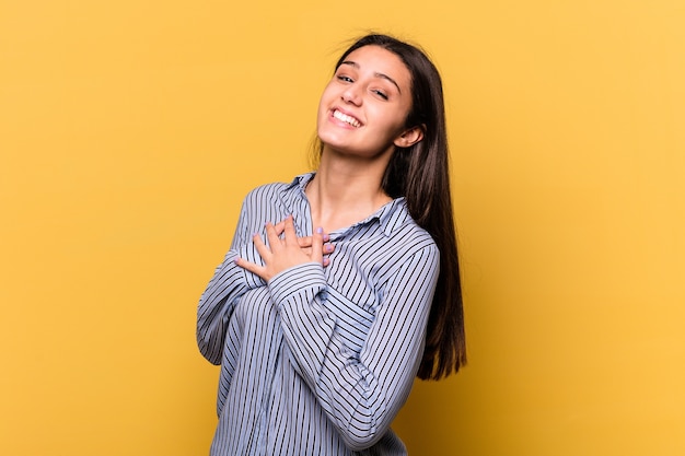 Jovem mulher indiana isolada em fundo amarelo tem uma expressão amigável, pressionando a palma da mão no peito. Conceito de amor.