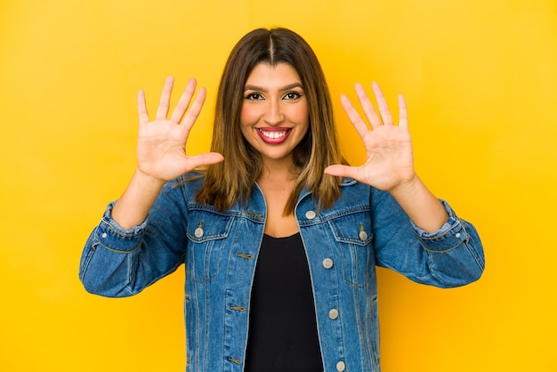 Jovem mulher indiana isolada na parede amarela, mostrando o número dez com as mãos.