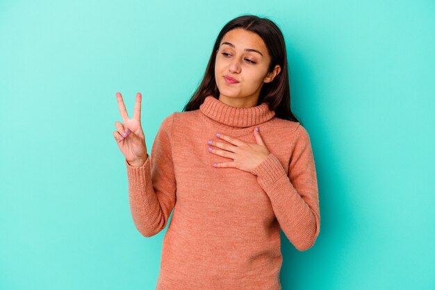 Jovem mulher indiana isolada na parede azul, fazendo um juramento, colocando a mão no peito.