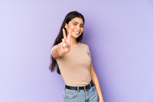 Jovem mulher indiana isolada na parede roxa, mostrando sinal de vitória e sorrindo amplamente.