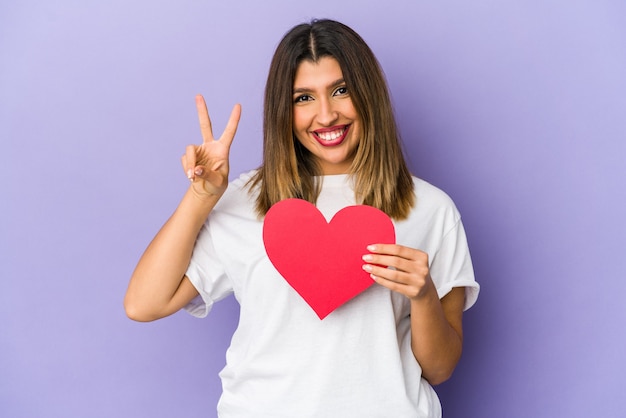 Jovem mulher indiana segurando um coração de dia dos namorados isolado mostrando o número dois com os dedos.