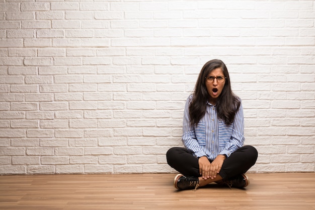 Jovem mulher indiana sente-se contra uma parede de tijolos muito irritado e chateado, muito tenso, gritando fu
