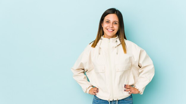 Jovem mulher isolada em azul seguro mantendo as mãos nos quadris.