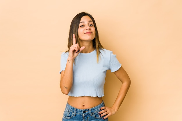 Jovem mulher isolada em bege, mostrando o número um com o dedo.