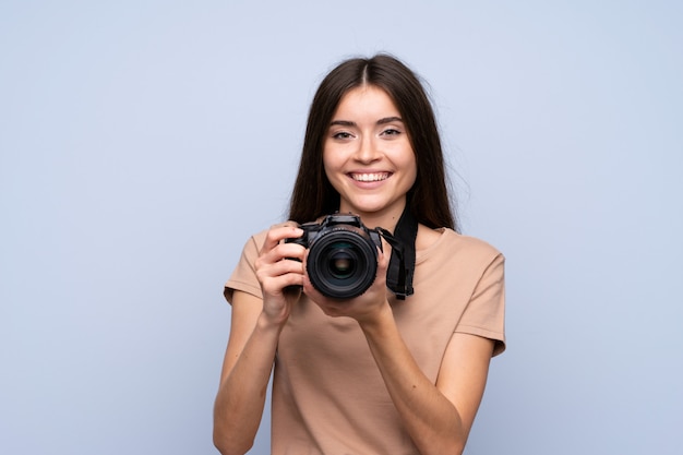 Jovem mulher isolada parede azul com uma câmera profissional