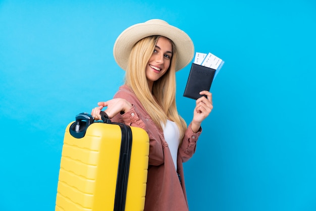 Jovem mulher isolada parede azul em férias com mala e passaporte