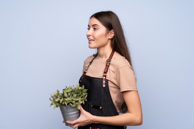 Jovem mulher isolada parede azul tomando um vaso de flores