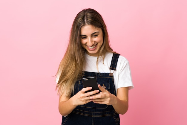 Jovem mulher isolada parede rosa, enviando uma mensagem com o celular