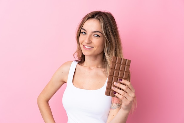 Jovem mulher isolada parede rosa tomando um comprimido de chocolate e feliz