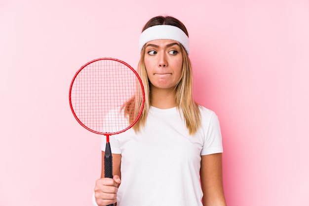 Jovem mulher jogando badminton isolado confuso, sente-se duvidoso e inseguro.