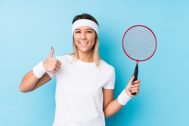 Jovem mulher jogando badminton, sorrindo e levantando o polegar