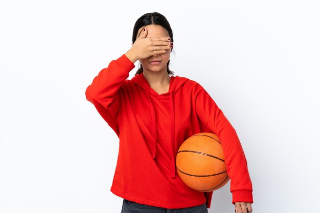 Jovem mulher jogando basquete na parede branca isolada, cobrindo os olhos pelas mãos. Não quero ver nada