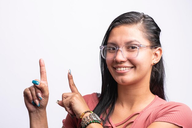 Foto jovem mulher latina com óculos sorridentes apontando no fundo branco