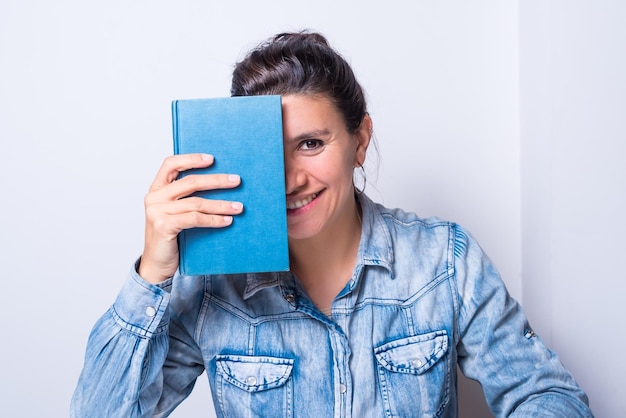 Jovem mulher latina com um livro fechado cobrindo metade do rosto sorrindo olhando para a frente